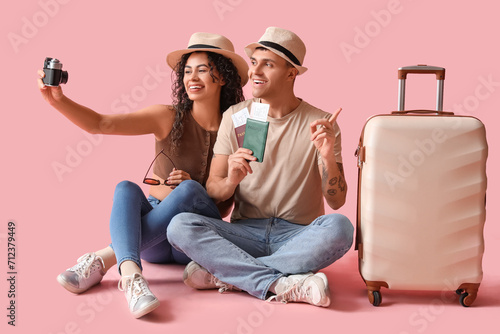 Couple of tourists with suitcase and passports taking selfie on pink background photo