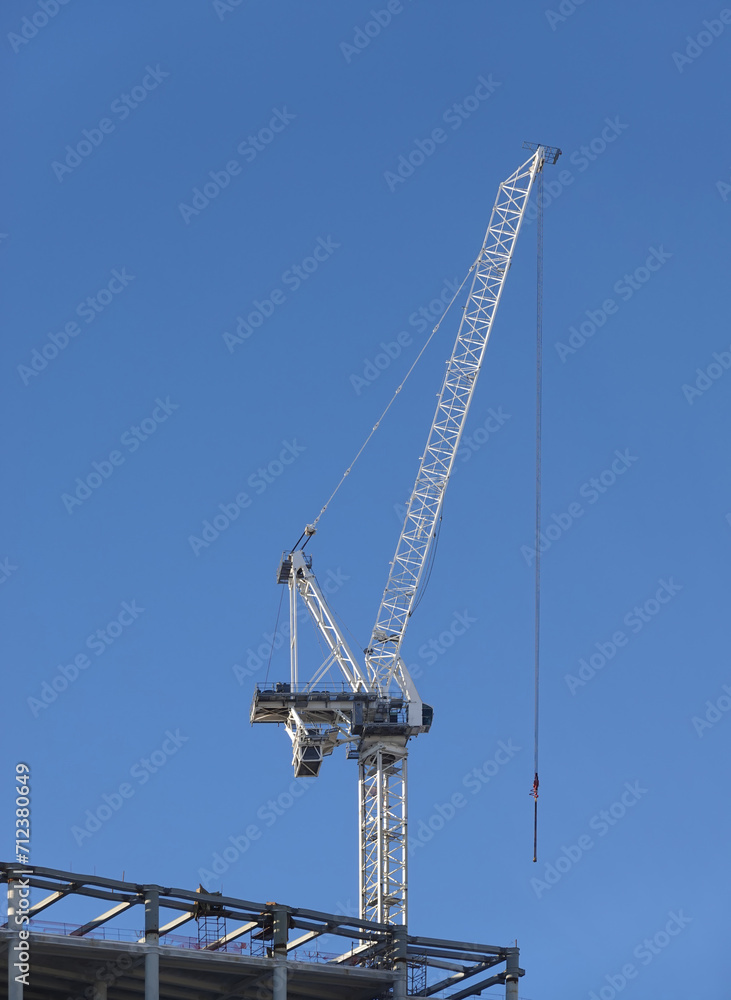 Hoisting tower crane on the top section being constructed of modern high skyscraper building against blue cloudless sky Hoisting tower crane on the top section being constructed of modern high skyscraper building against blue cloudless sky