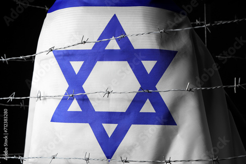 Jewish woman with flag of Israel behind barbed wire on black background, back view. International Holocaust Remembrance Day photo