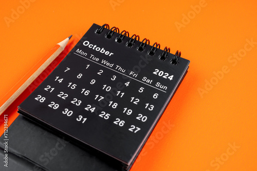 October 2024 desk calendar with pencil on orange background.