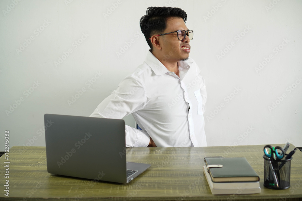 young asian businessman in a workplace suffering from backache for having made an effort wear white shirt with glasses isolated young asian businessman in a workplace suffering from backache for having made an effort wear white shirt with glasses isolated