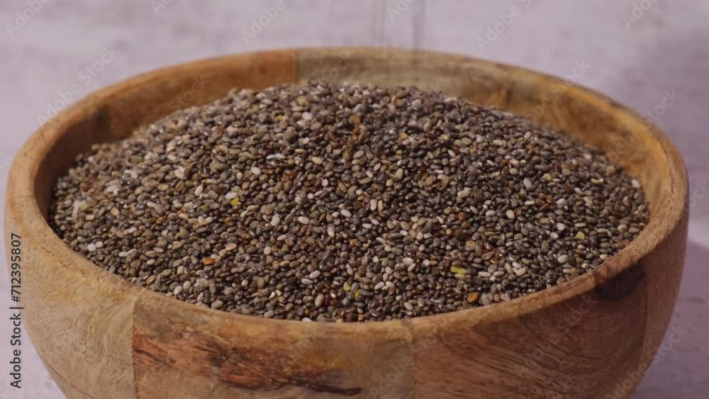 Slow motion chia seeds fall in wooden bowl. Healthy superfood rich in Omega 3 fatty acids. Dry healthy natural ingredient. Chia grains are falling. Vegetarian food Slow motion chia seeds fall in wooden bowl. Healthy superfood rich in Omega 3 fatty acids. Dry healthy natural ingredient. Chia grains are falling. Vegetarian food