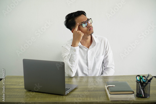 young asian businessman in a workplace looking up thinking finger touching head wear white shirt with glasses isolated