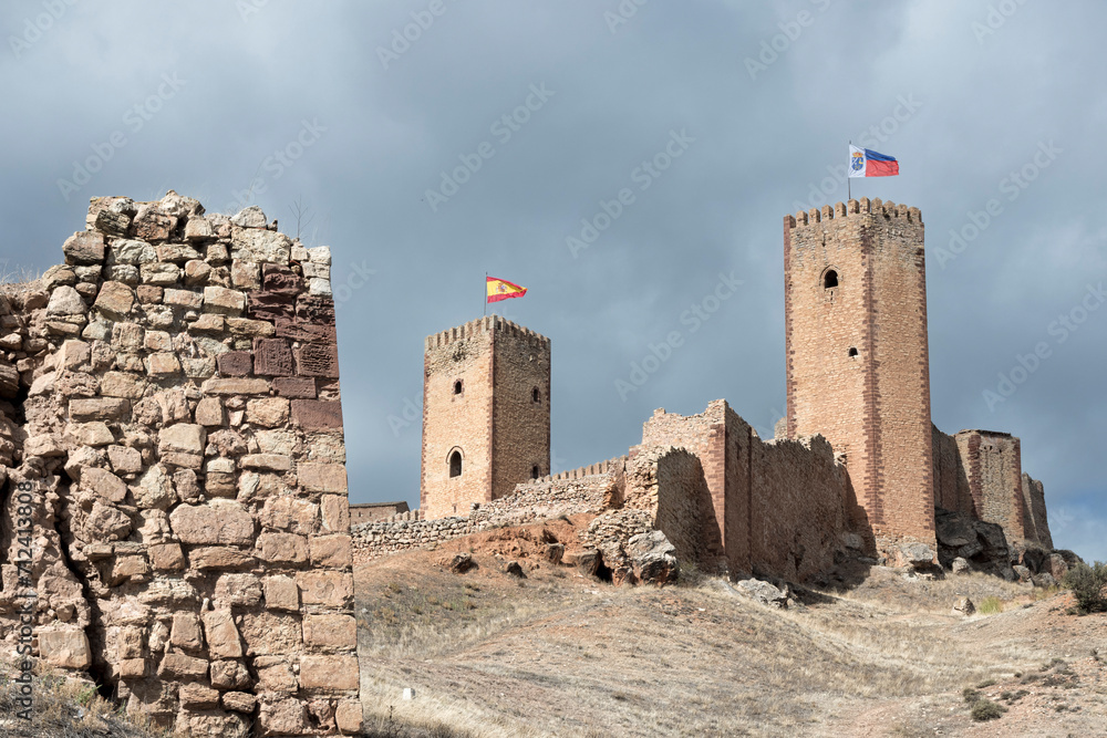 an ancient stone castle with two towers, each flying a different flag, under a cloudy sky