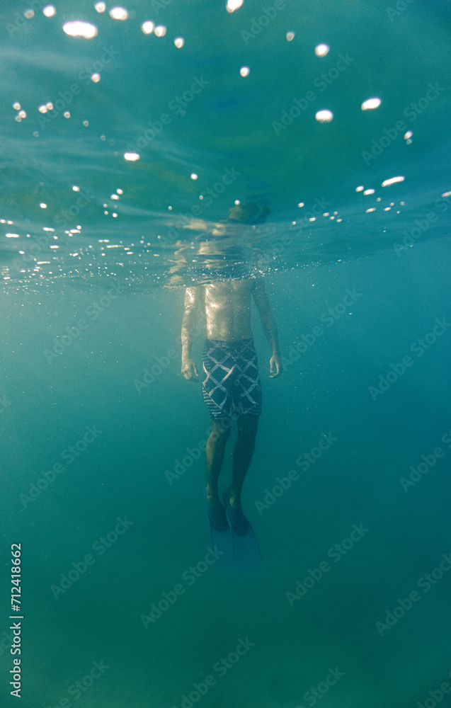 Body of a Man underwater with sunlight shining down on him. clear blue water with bubbles. Surreal scene. Creative