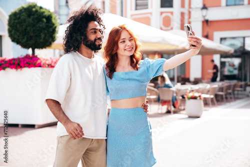 Smiling beautiful redhead  woman and her handsome boyfriend. Model in casual summer clothes. Happy cheerful family. Female having fun. Couple posing in the street at sunny day. Take selfie