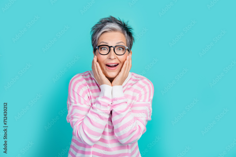 Photo of impressed funky lady wear striped sweater spectacles arms hands cheeks empty space isolated turquoise color background