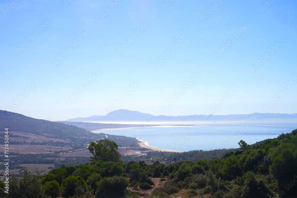 view from a mountain along the coastline of the Costa de la Luz, Andalusia, Spain with the mountains of Morocco behind the Strait of Gibraltar at the horizon view from a mountain along the coastline of the Costa de la Luz, Andalusia, Spain with the mountains of Morocco behind the Strait of Gibraltar at the horizon