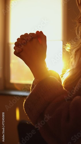 close-up of female hands palm to palm. the girl prays in front of the window at sunset. vertical video