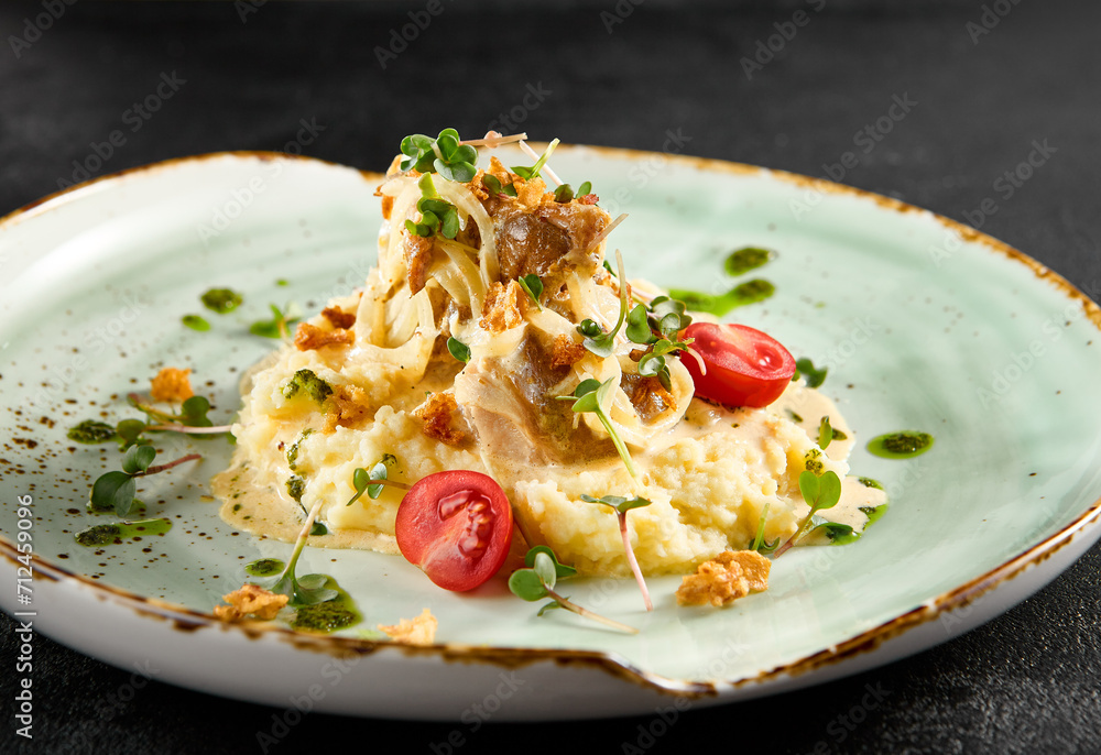 Creamy mashed potatoes topped with tender squid and caramelized onions, garnished with cherry tomatoes on a speckled turquoise plate Creamy mashed potatoes topped with tender squid and caramelized onions, garnished with cherry tomatoes on a speckled turquoise plate