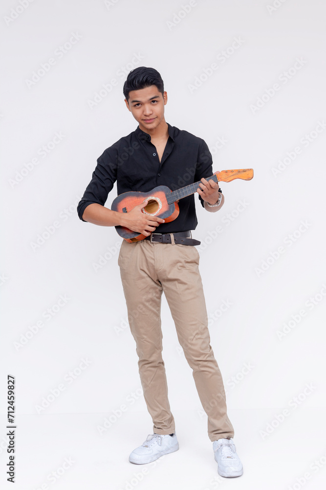 A young handsome and dapper asian male playing the ukulele. Full body photo, isolated on a white background.