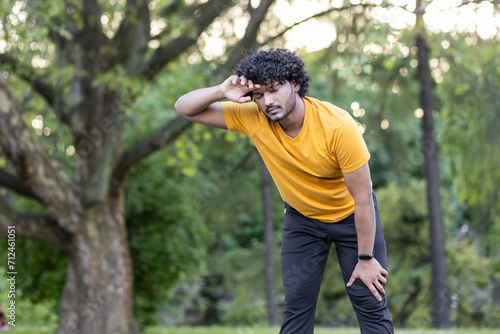 Active indian man in sportswear taking a break during a workout in a green park