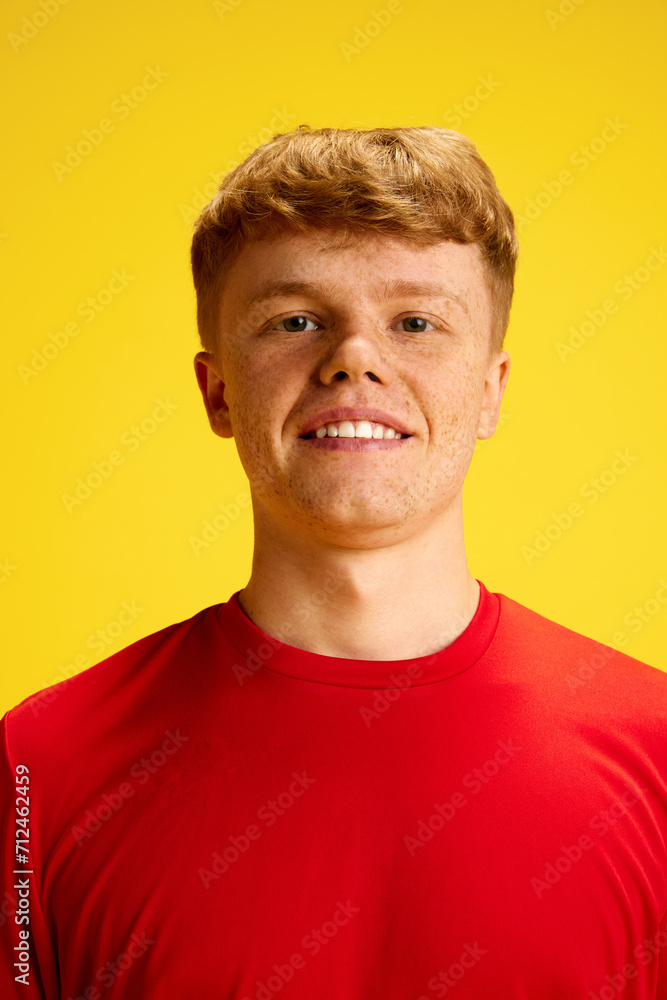Portrait of young redhead man with freckles, wearing red t-shirt, smiling, looking at camera against yellow studio background. Concept of active lifestyle, youth, hobby and human emotions Portrait of young redhead man with freckles, wearing red t-shirt, smiling, looking at camera against yellow studio background. Concept of active lifestyle, youth, hobby and human emotions