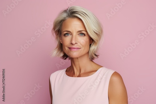 Beautiful middle aged woman looking at camera and smiling while standing against pink background