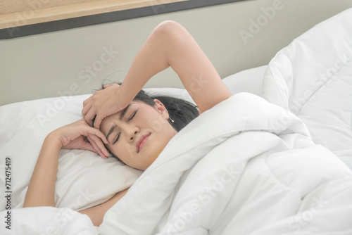 Young woman white lying sheets in a bed with is suffering from headaches. female trying to comfort her pain by holding her hands against her forehead. health headache problem concept. out of focus.