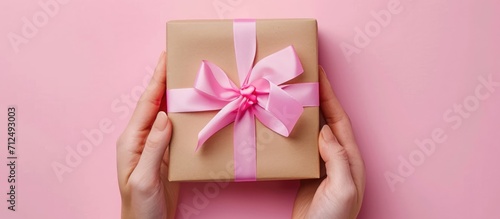 Female hand holding a gift box with a pink ribbon. Congrats on the holiday.