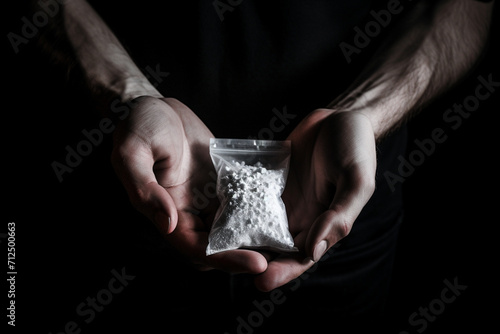 Packet with white narcotic in hand on black background, monochrome 