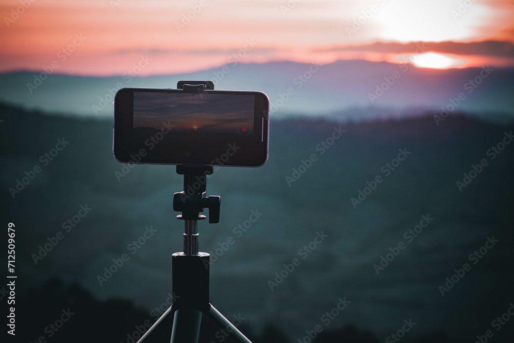 A smartphone is recording the sun setting over a mountain range. A smartphone is recording the sun setting over a mountain range.