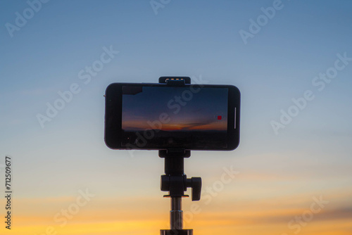 A smartphone is recording the sun setting over a mountain range.