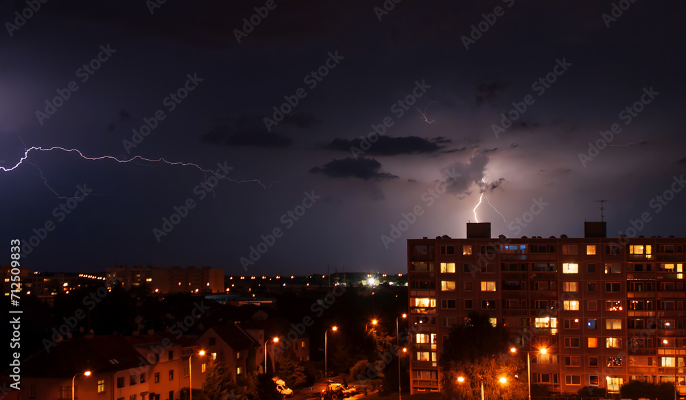 Evening thunderstorm lightning over the city. Background with summer thunder and gale over illuminated housing estate.