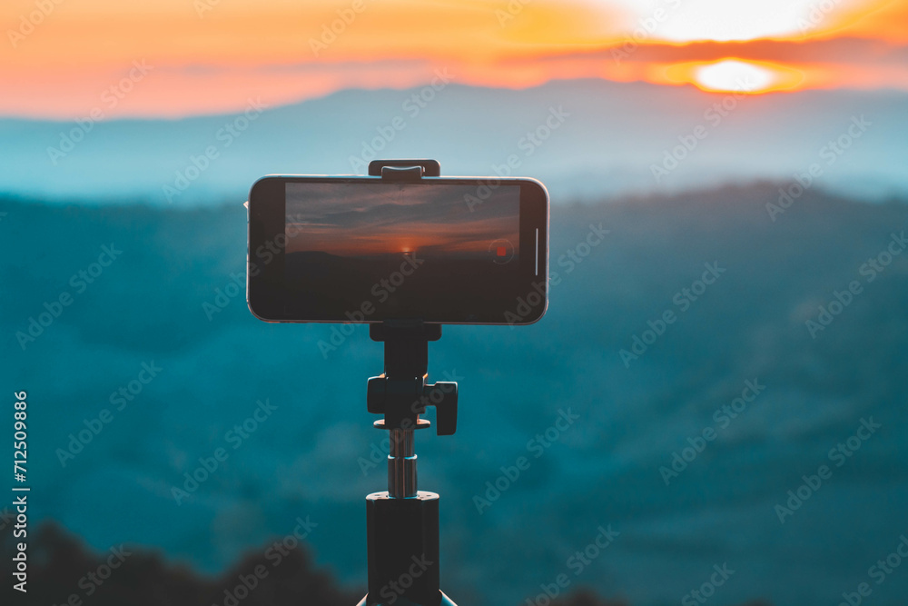A smartphone is recording the sun setting over a mountain range. A smartphone is recording the sun setting over a mountain range.