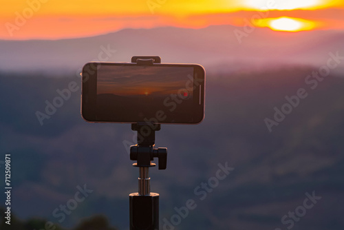 A smartphone is recording the sun setting over a mountain range.