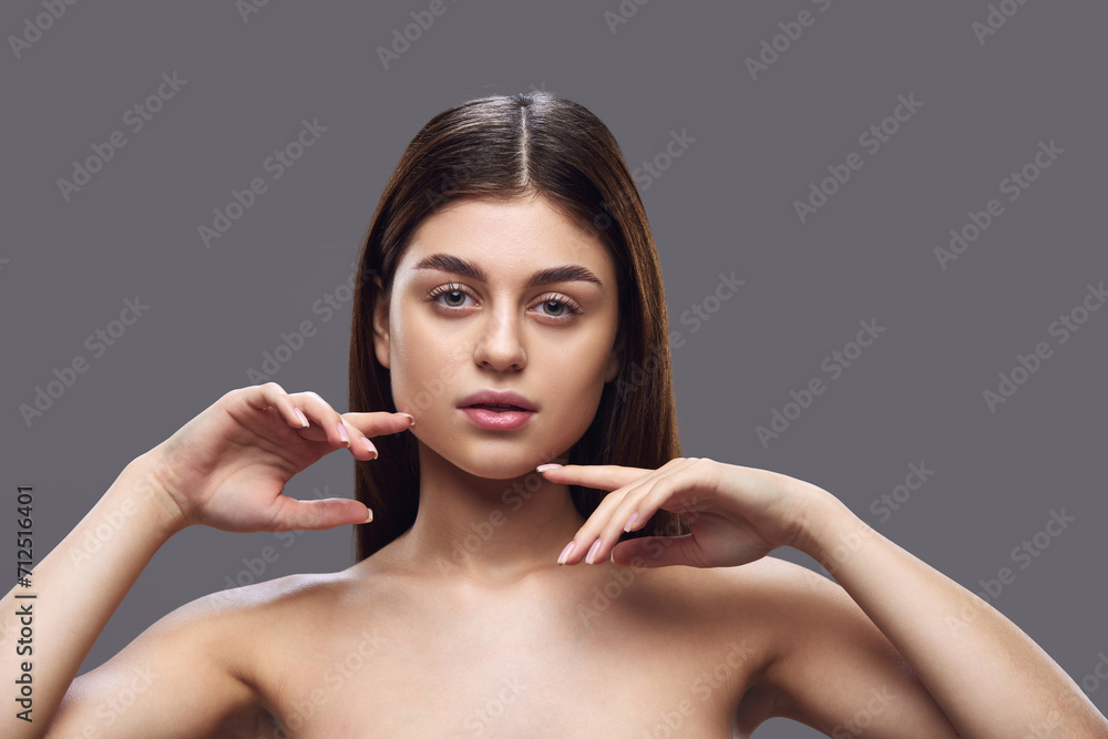 Young attractive, tender lady with neutral make up posing looking at camera against grey studio background. Concept of skin care product line featuring cleansers and moisturizers for clear complexion. Young attractive, tender lady with neutral make up posing looking at camera against grey studio background. Concept of skin care product line featuring cleansers and moisturizers for clear complexion.