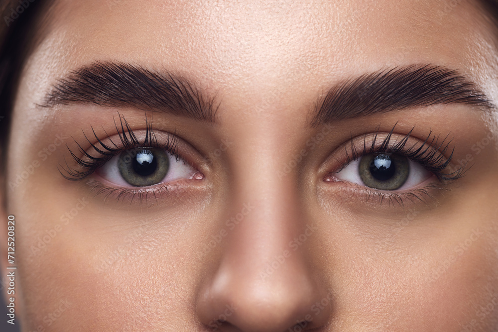 Fototapeta premium Cropped portrait of young attractive girl with smooth fresh skin. female face, bright eyes, long lushes and brows. Concept of anti-aging skincare cosmetic products that target delicate under-eye area.