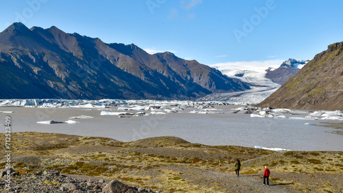 Hikers make their way to the edge of glacial lake at melting Vatnajokull glacier, warming fue to climate change, Iceland
