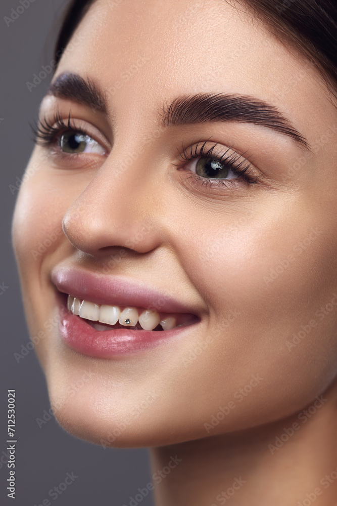 Close up portrait of female model face with with perfect lips and eye makeup smiling looking away against grey studio background. Concept of eyebrow styling product, natural beauty, full brows. Close up portrait of female model face with with perfect lips and eye makeup smiling looking away against grey studio background. Concept of eyebrow styling product, natural beauty, full brows.