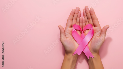 A hand holding a pink ribbon on a plain pink background. To commemorate World Cancer Day.