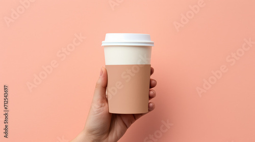 Female hand holding empty white blank paper cup of coffee with a cap. Isolated on tan background with copy space