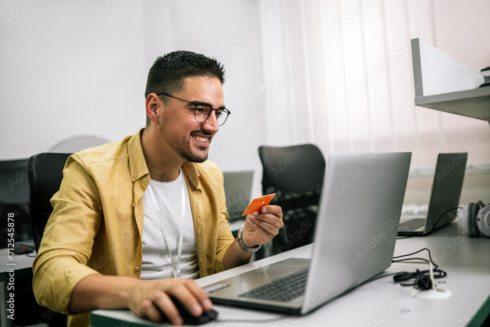 Happy cheerful smiling young adult man doing online shopping or e-shopping Happy cheerful smiling young adult man doing online shopping or e-shopping