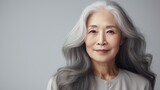 Elegant, smiling, elderly, chic Asian woman with gray long hair and perfect skin, on a gray background, banner