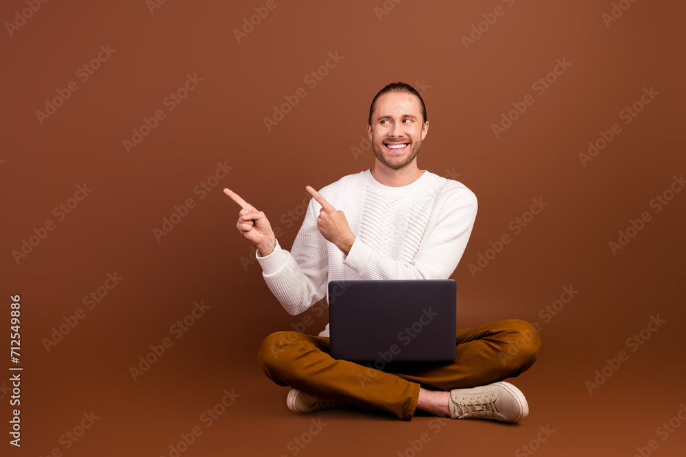 Full length photo of cheerful dreamy guy dressed white pullover typing modern gadget two fingers empty space isolated brown color background Full length photo of cheerful dreamy guy dressed white pullover typing modern gadget two fingers empty space isolated brown color background