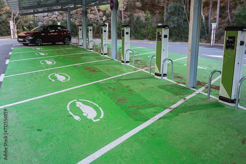 A row of electric vehicle charging stations marked by green paint on the pavement with a solar panel roof overhead photo