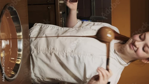 Female confectioner demonstrates right consistence of molten chocolate for dessert manufacturing. Cook pours fluid chocolate into stainless container