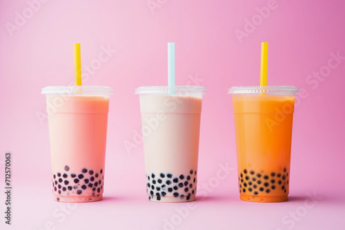 Yellow and pink milk bubble tea in transparent plastic cups and straws standing in line on blush pink background.