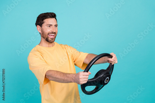 Photo of young optimistic brunet hair guy in yellow t shirt driving rent automobile to travel europe isolated on cyan color background
