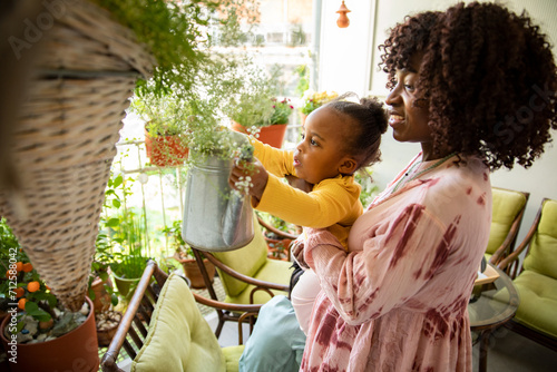 Mother and toddler daughter watering home plants photo