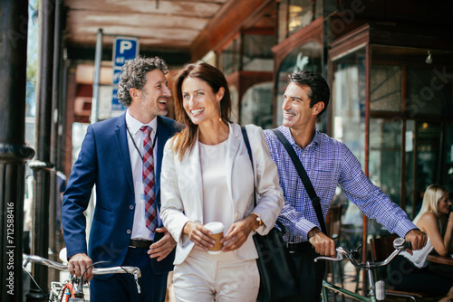 Business colleagues laughing and walking together in the city with coffee and a bicycle photo