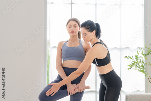 Two women confident training yoga. Athletic women in sportswear doing fitness stretching exercises at home in the living room. Sport and recreation concept. Yoga teacher is helping young woman. © ultramansk