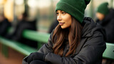 Mulher jovem com gorro verde sentada em banco de parque