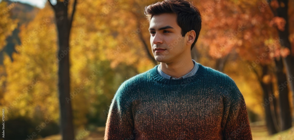 a young man standing in front of a tree filled with orange and yellow leaves in a park with a green sweater and a red and yellow and orange tree in the background. a young man standing in front of a tree filled with orange and yellow leaves in a park with a green sweater and a red and yellow and orange tree in the background.