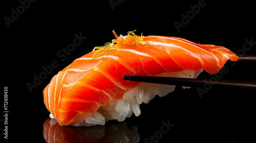 Close up of delicious and fresh salmon nigiri being lifted by black chopstick. Sushi presented on a black background creating dramatic contrast.