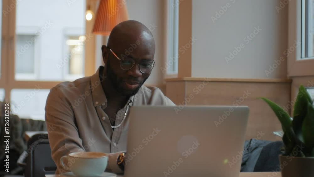 Confident young African American man looking at webcam and making a video call. Happy man talking and waving, having an online video chat interview, sitting at the table. Confident young African American man looking at webcam and making a video call. Happy man talking and waving, having an online video chat interview, sitting at the table.