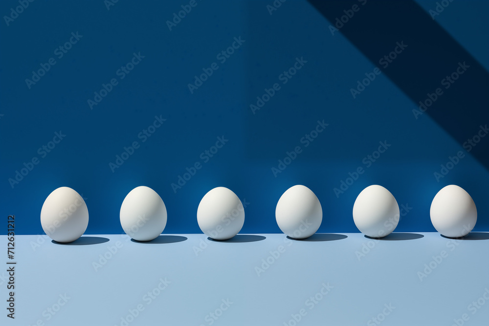A row of white eggs perfectly aligned against a deep blue blue background, embodying a minimalist and clean aesthetic.
A row of white eggs perfectly aligned against a deep blue blue background, embodying a minimalist and clean aesthetic.