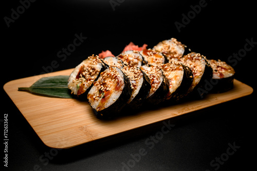 Side view of sushi rolls covered with sauce and sprinkled with sesame seeds