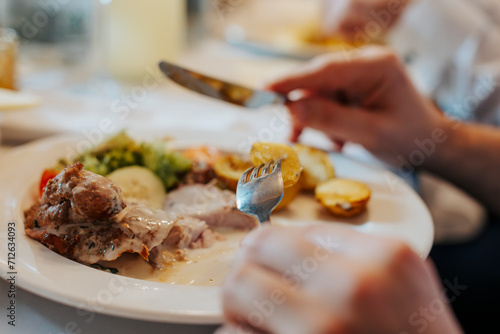 A person is eating dinner at the table using cutlery, close-up on hands and plate full of food