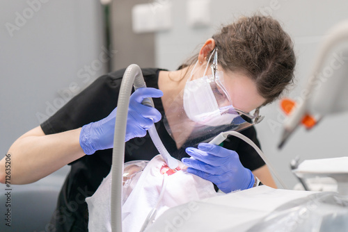 A female dentist performs a dental procedure for a patient, cleaning her teeth from plaque and tartar using an air abrasion device. Aesthetic dentistry and dental care.